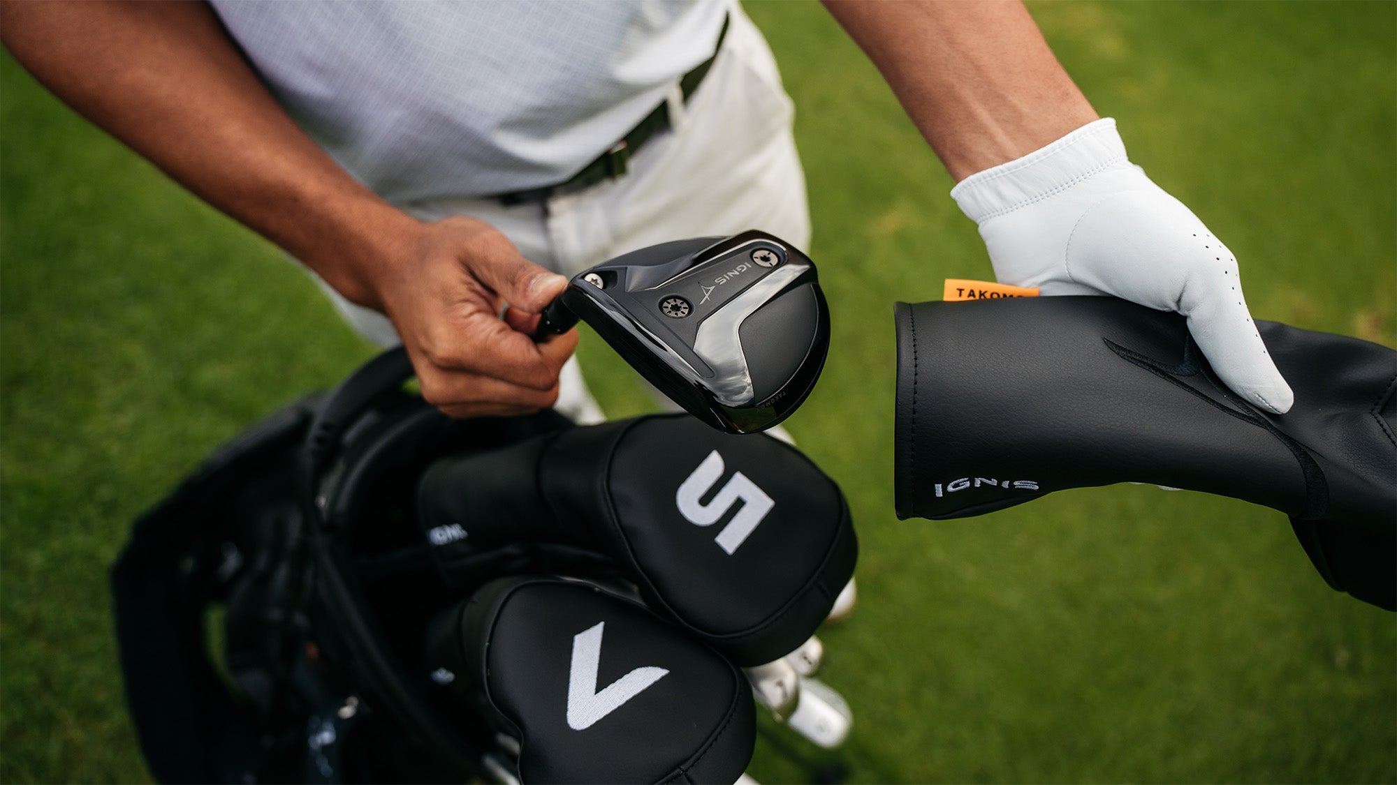 Person holding a fairway wood with Takomo logos on a grassy background
