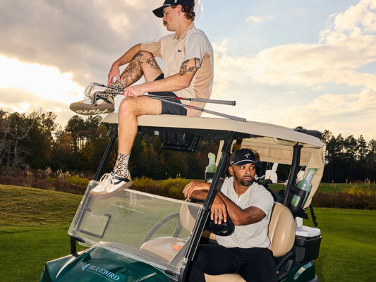 Two golfers relaxing on a golf cart, with one sitting on the roof and another in the driver’s seat