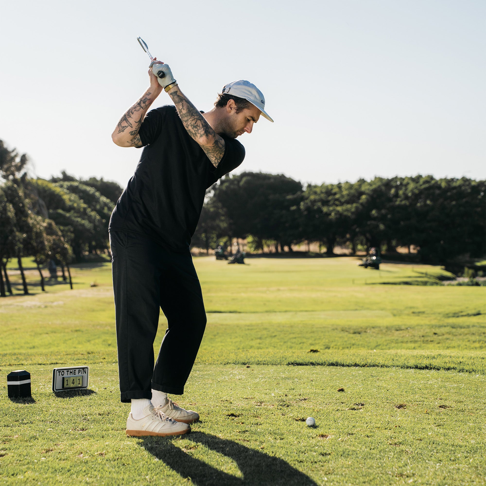 Person playing golf on a sunny day with trees in the background