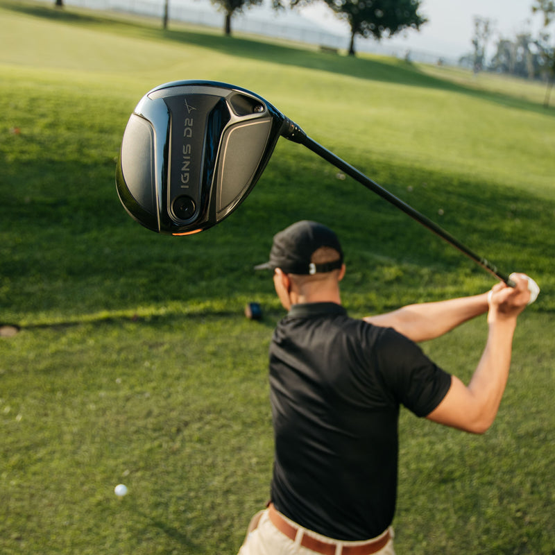 A golf club head floating in the foreground with a golfer seen from behind on a grassy golf course. The club is branded IGNIS D2.