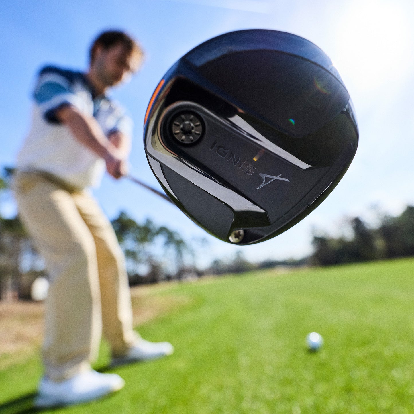 Golf club head with 'IGNIS' branding in front of a golfer on a course