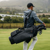 Man carrying a black golf bag on a golf course