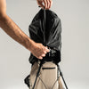 Person closing a black rain cover over a golf bag against a plain background