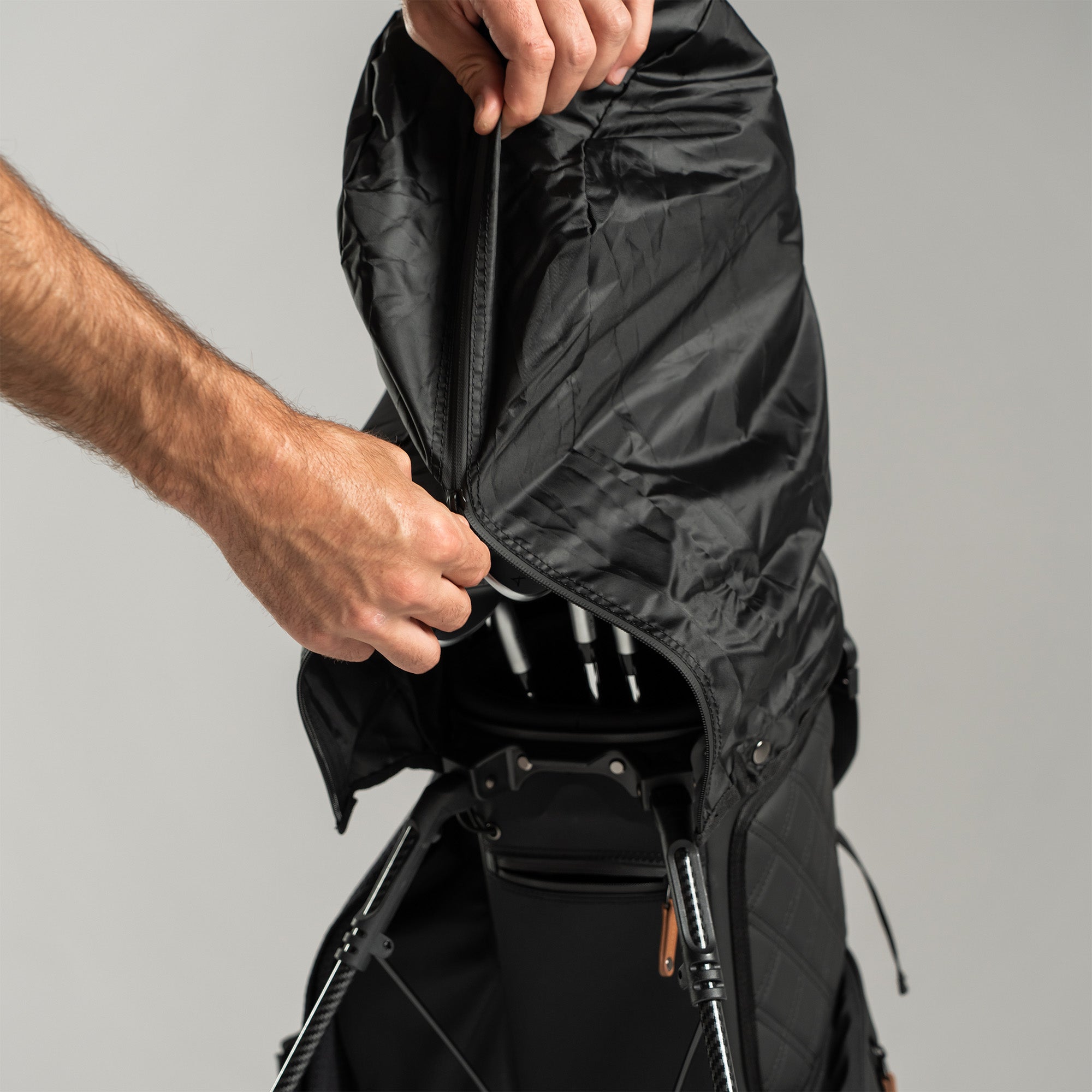 Person closing a golf bag's black raincoat