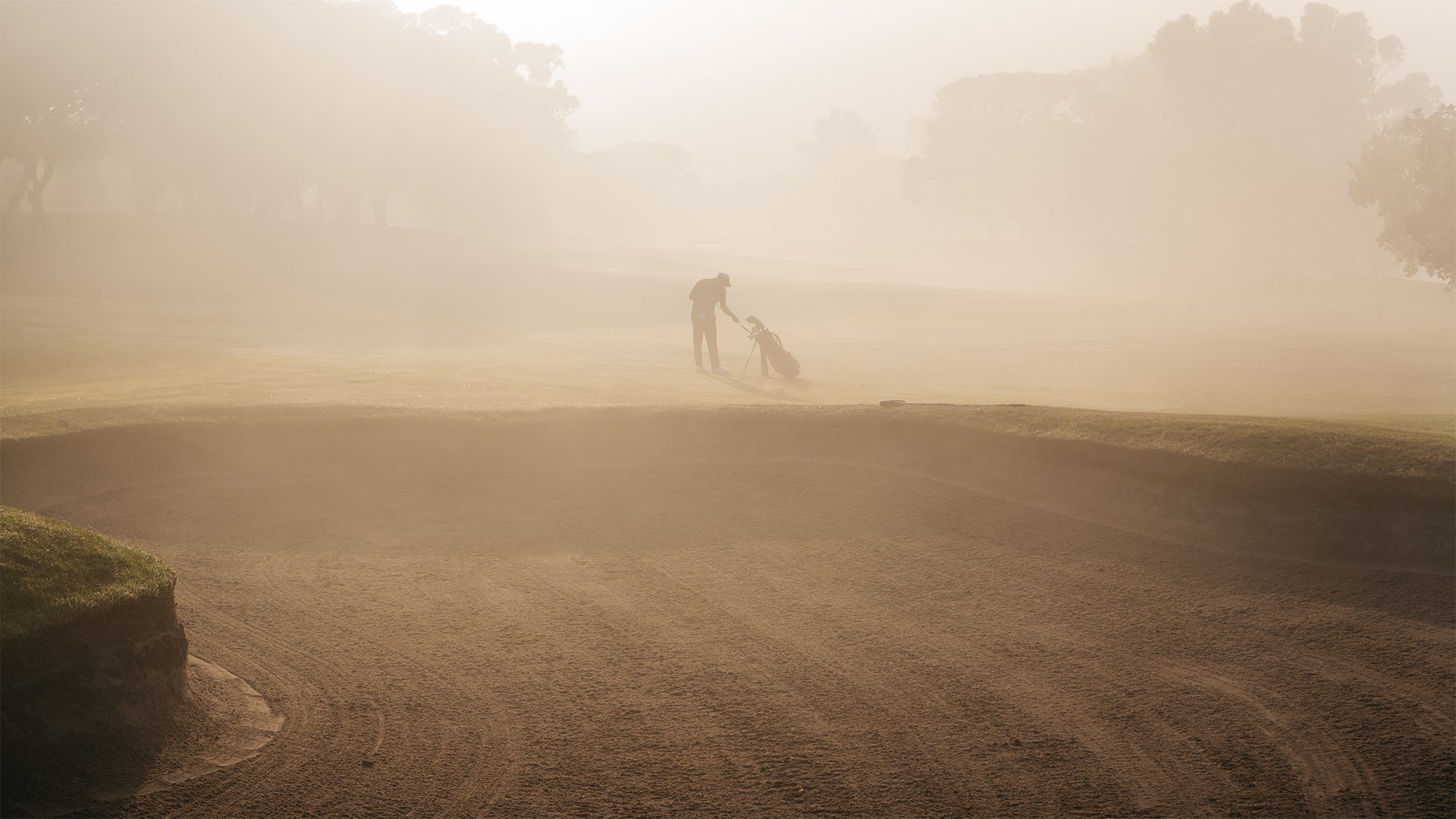 A man pulling a golf club from his golf bag at a misty golf course