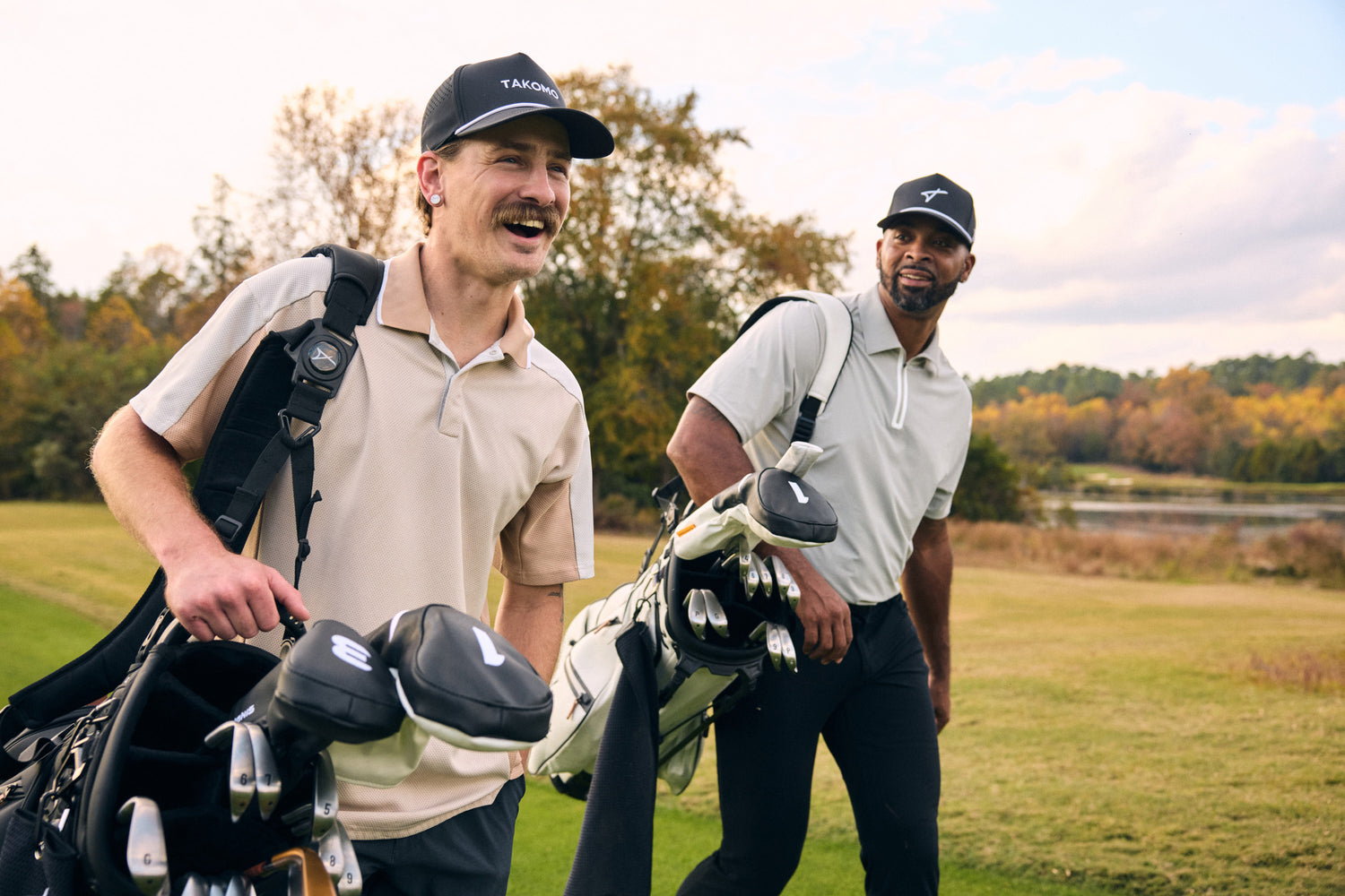 Two men having a joyful conversation on a golf course while carrying Takomo golf bags and wearing Takomo caps.