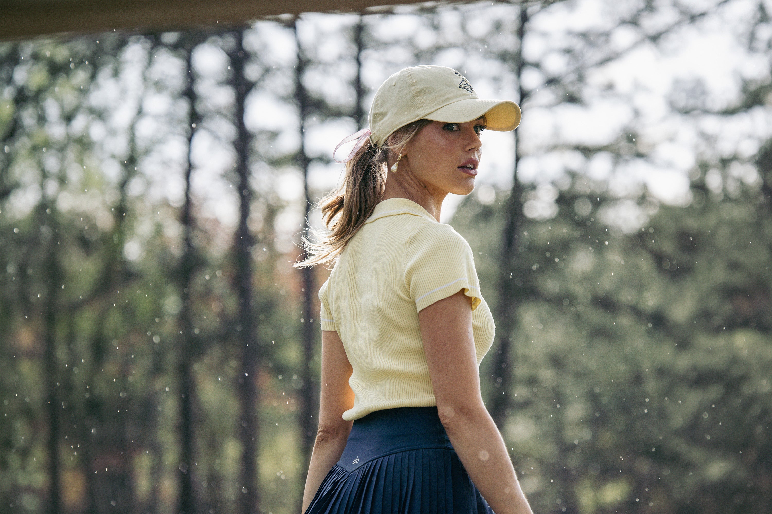 Woman in a yellow shirt and cap walking outdoors with trees in the background