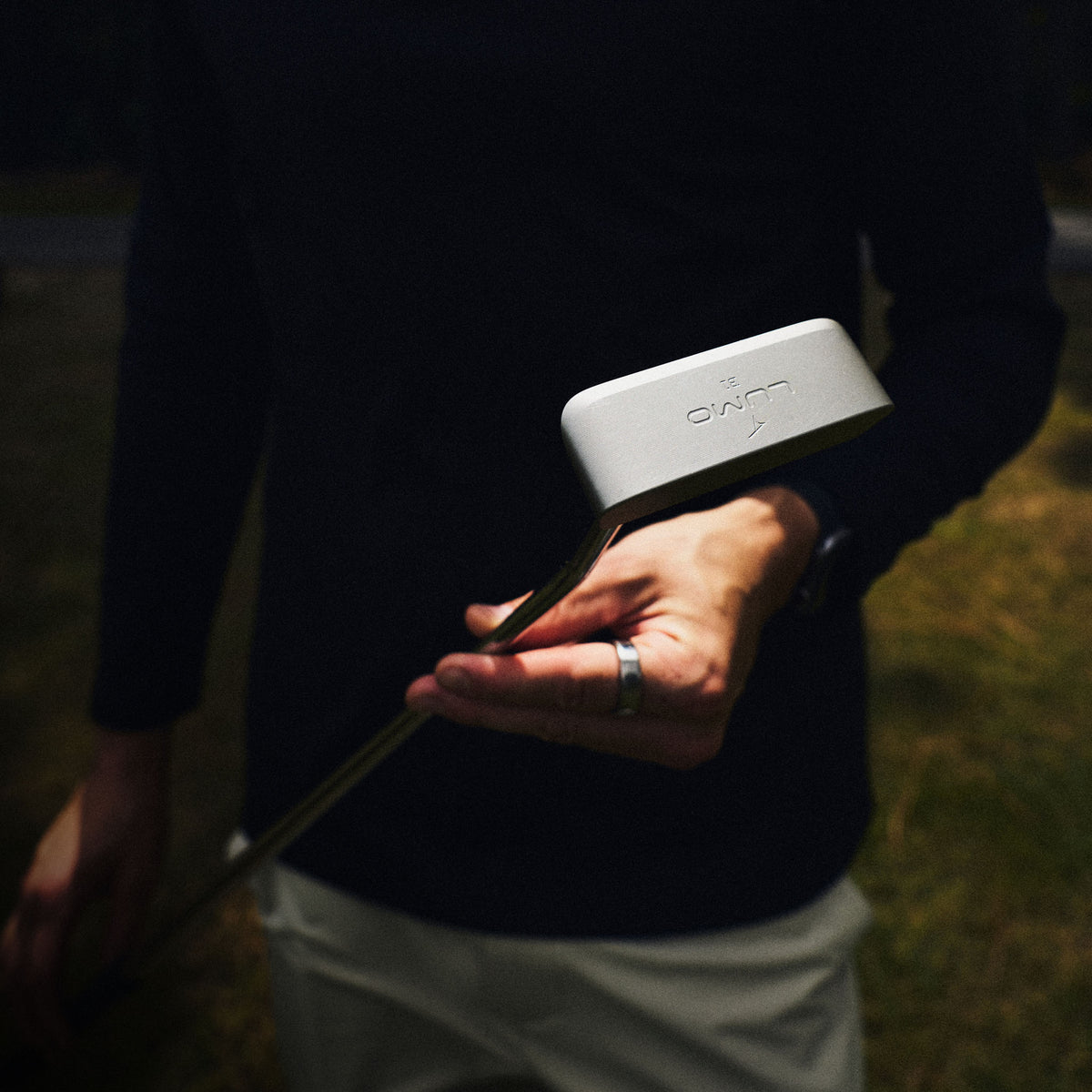 Takomo LUMO B1 blade putter held by a golfer in high-contrast lighting outdoors. 