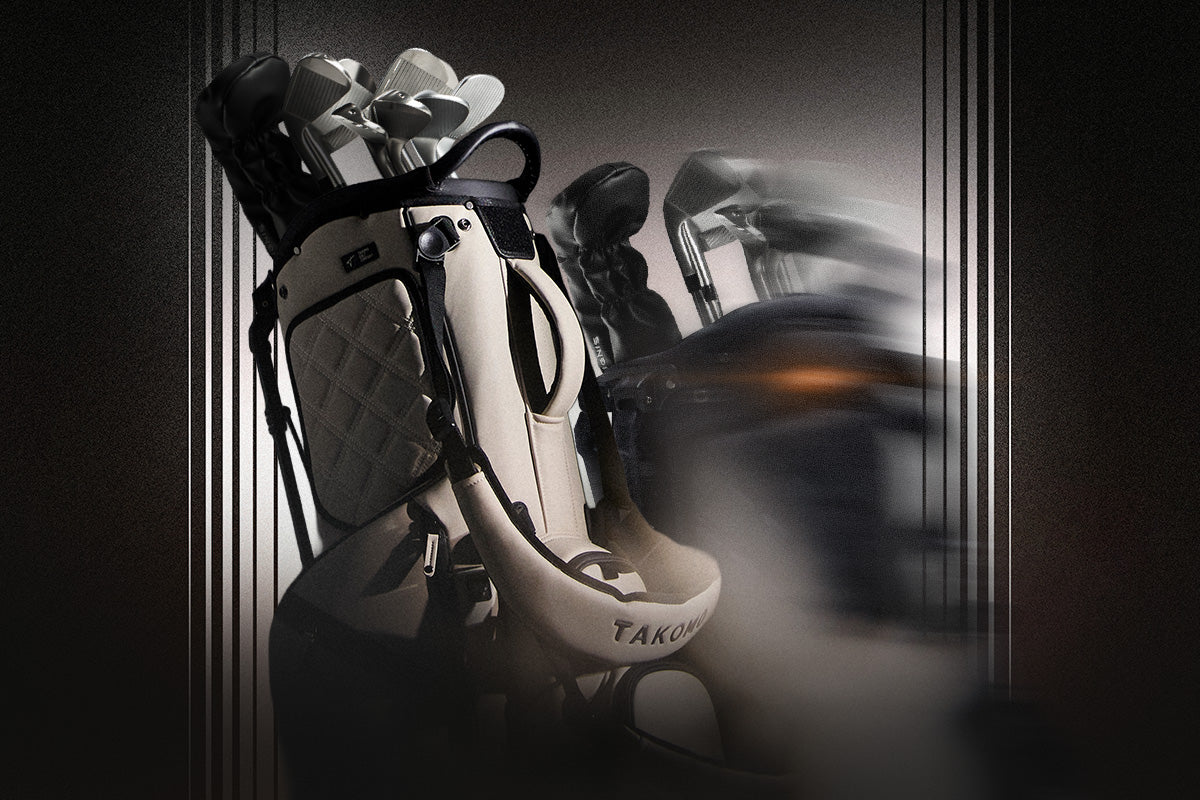 A white and black Takomo golf bag filled with golf clubs, shown in a moody, dark studio setting with a blurred, motion-like secondary bag in the background.