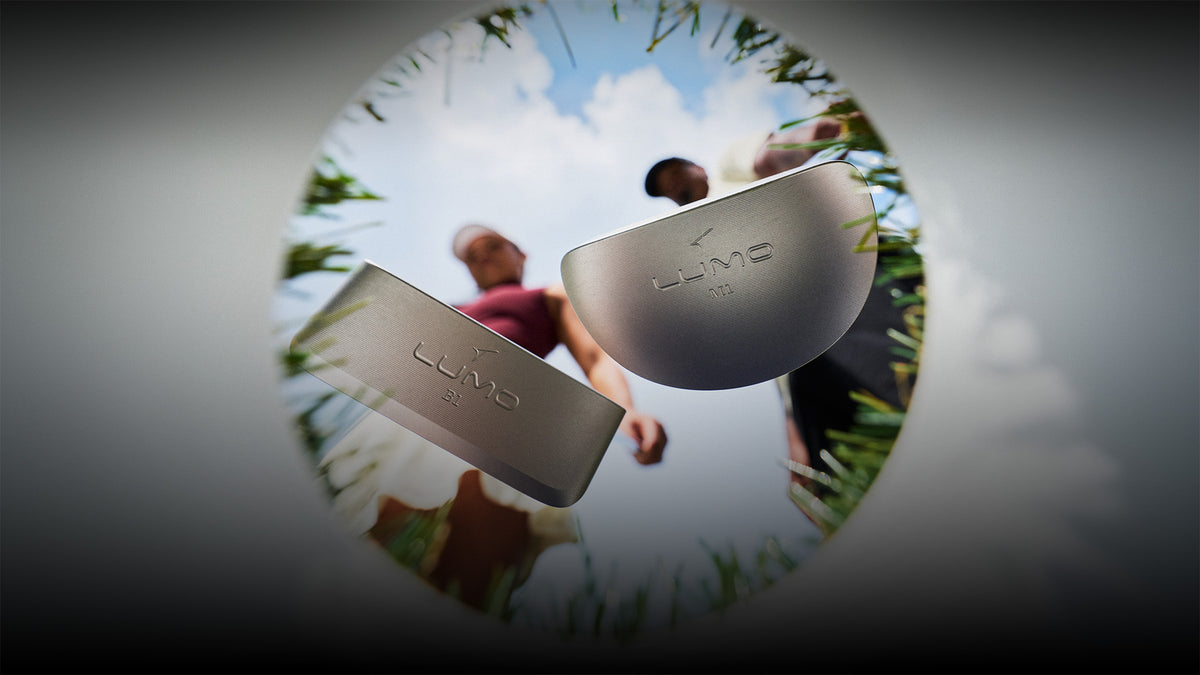 Two Takomo Lumo putters hovering above a golf hole, captured from below.
